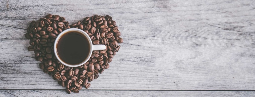 coffee beans in a heart shape with a mug of black coffee sitting on top